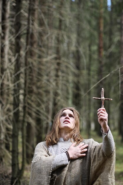 Un hombre con una sotana pasa un ritual en un bosque oscuro con una bola de cristal y un libro.