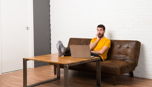 Hombre con su computadora portátil en una habitación sorprendida y sorprendida mientras mira a la derecha