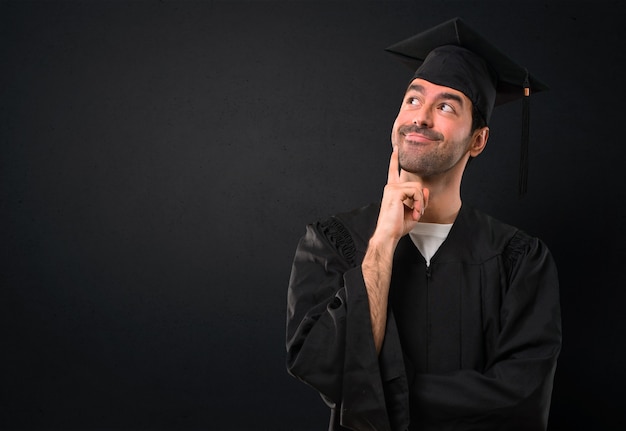 Hombre en su día de graduación Universidad de pie y pensando en una idea mientras mira hacia arriba