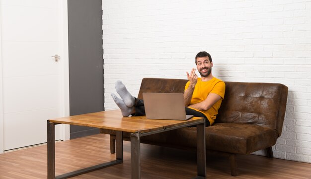 Hombre con su laptop en una habitación invitando a venir con la mano. Feliz de que hayas venido