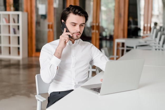 Hombre en su lugar de trabajo con teléfono y computadora portátil en la oficina