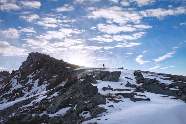 El hombre sube a la cima de la montaña hacia el sol en el paisaje de búsqueda.