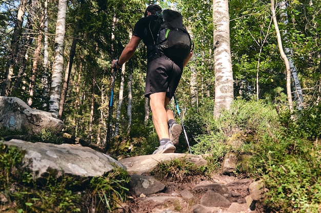 El hombre sube en zapatillas de deporte en acción al aire libre. Vista superior de la bota de senderismo en el sendero. Piernas de primer plano en jeans y zapatos deportivos de trekking sobre piedras rocosas del bosque de montaña.