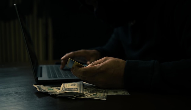 hombre en una sudadera con capucha usando una computadora portátil para hackear información financiera de tarjetas de crédito