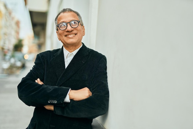 Hombre del sudeste asiático de mediana edad sonriendo confiado con los brazos cruzados apoyado en la pared