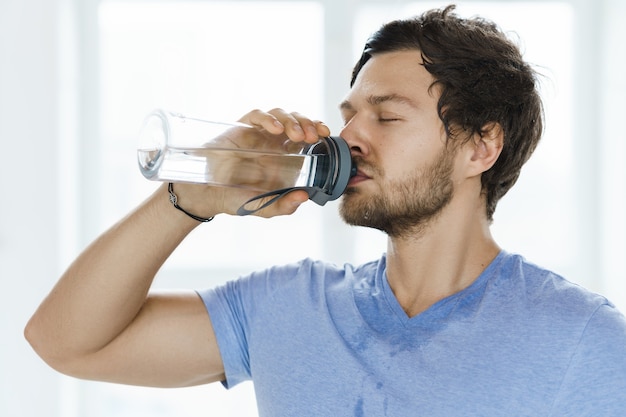 Hombre sudoroso cansado bebe agua después del entrenamiento físico en el gimnasio