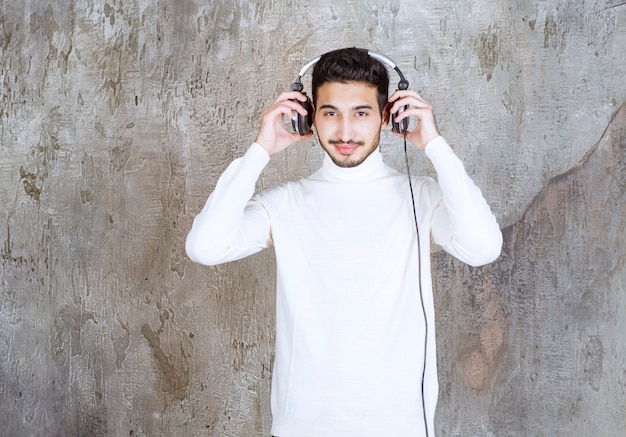 Hombre de suéter blanco con auriculares y escuchando música.