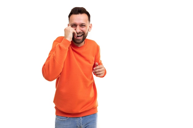 Un hombre con un suéter naranja se ríe con las manos en el estómago y la cara sobre un fondo blanco.