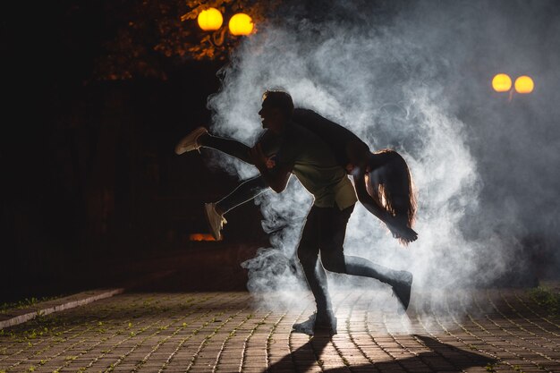 El hombre sujeta a una mujer en la calle oscura con un humo. Noche