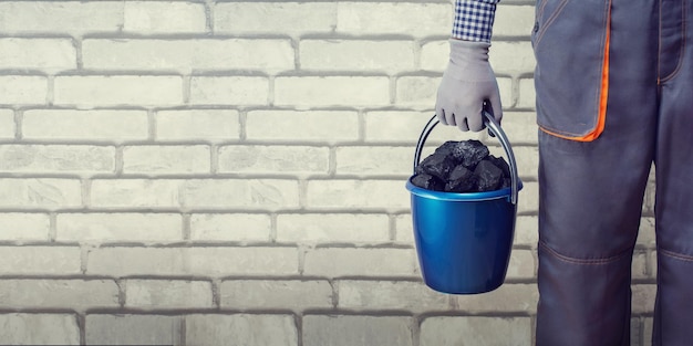 Hombre sujetando un balde con carbón contra la pared de fondo de ladrillo vendiendo la compra de un cartel de concepto de carbón con espacio de copia