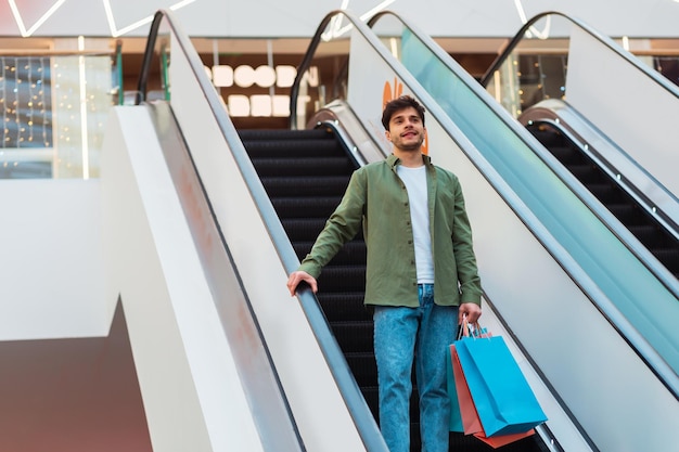 Hombre sujetando bolsas de compras de pie en las escaleras móviles en el centro comercial