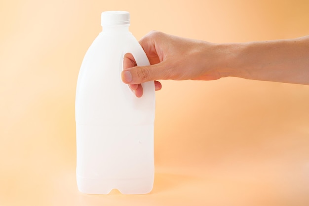 Hombre sujetando una botella de un galón de leche sobre un fondo naranja Persona Tienda Orgánica Natural Vaca Objeto Limpio Único