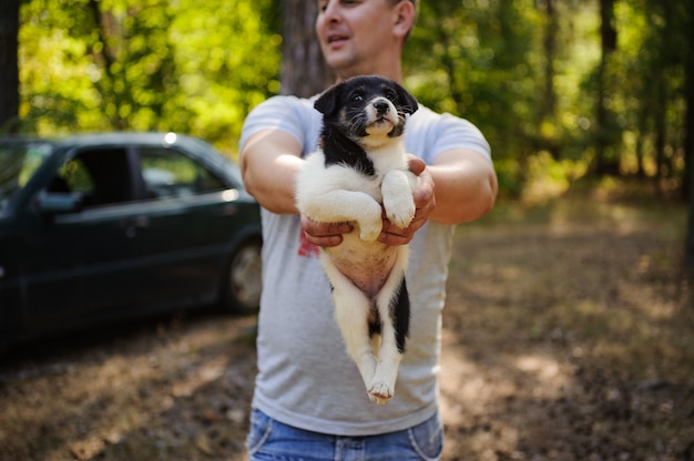 Hombre sujetando un cachorro blanco y negro en el bosque