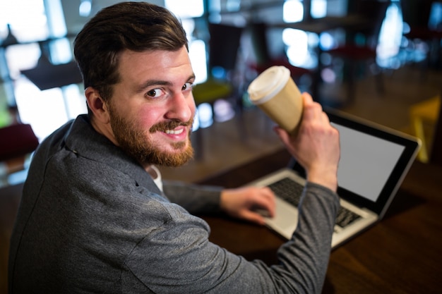 Hombre sujetando café mientras usa la computadora portátil