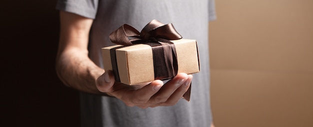 Hombre sujetando caja de regalo sobre fondo marrón