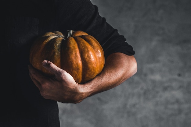 Hombre sujetando calabaza madura en manos sobre un fondo gris