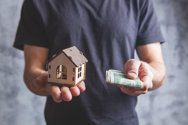 Hombre sujetando una casa y dinero en un gris