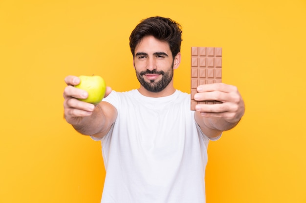 Hombre sujetando chocolate y manzana sobre pared aislada