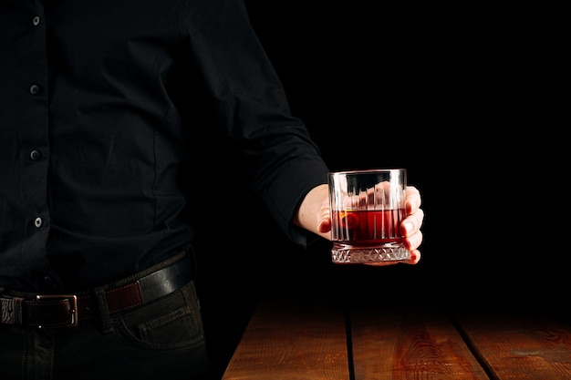 Hombre sujetando una copa de cóctel negroni sobre la mesa de madera