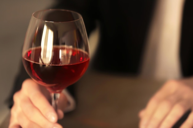 Hombre sujetando una copa con vino sobre fondo borroso