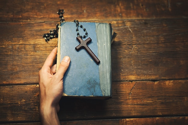 Hombre sujetando una cruz y biblia