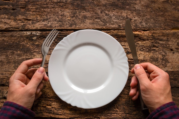 Hombre sujetando un cuchillo y un tenedor junto al plato sobre una madera