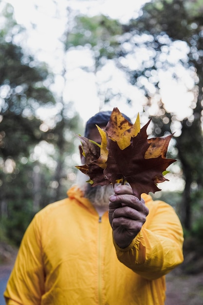 Hombre sujetando la hoja de otoño en la cara delantera