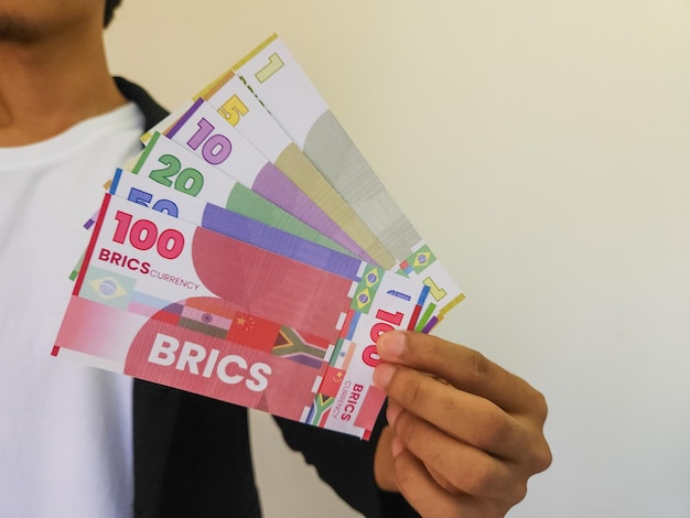 Hombre sujetando una ilustración de la moneda BRICS que podría sacudir el dominio del dólar