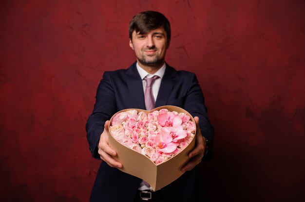 Hombre sujetando en una mano una caja de flores rosas