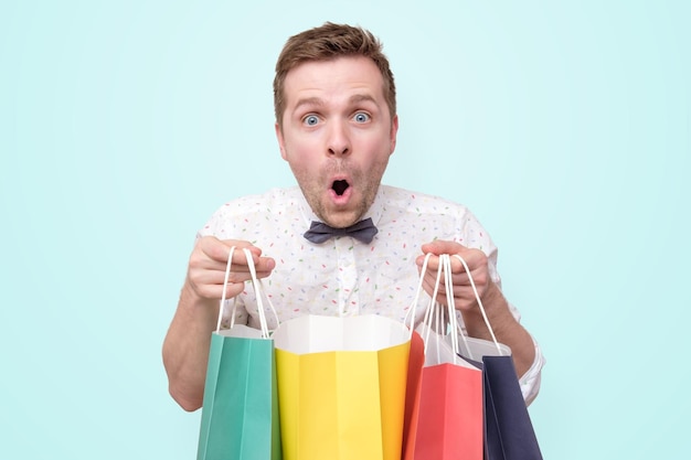 Hombre sujetando montones de bolsas con regalos con shock