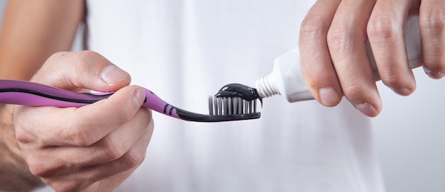 Hombre sujetando pasta de dientes negra y cepillo de dientes