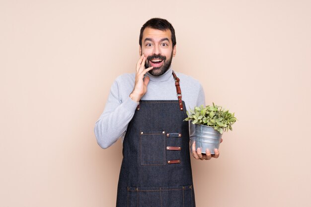 Hombre sujetando una planta aislada con sorpresa y conmocionada expresión facial