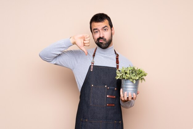 Hombre sujetando una planta sobre aislado mostrando el pulgar hacia abajo