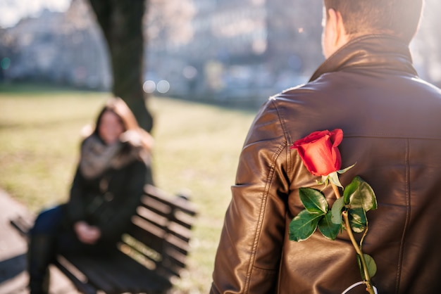 Hombre sujetando una rosa roja detrás de la espalda
