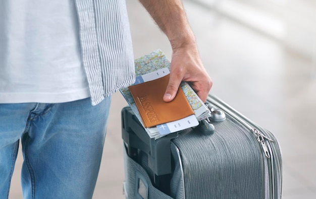 Hombre sujetando su pasaporte y llevando una maleta de cerca