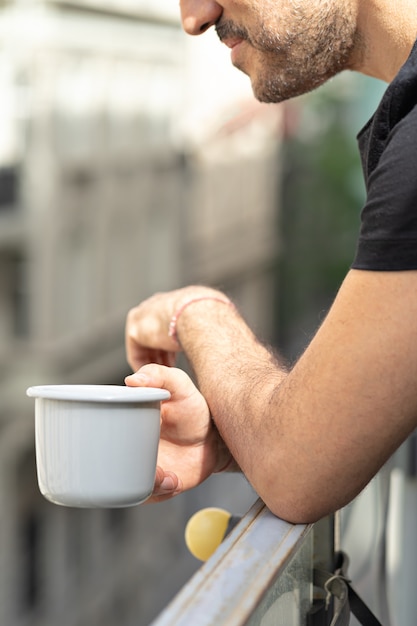 Hombre sujetando una taza de café en el balcón con vistas a la ciudad