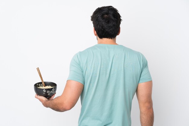 Hombre sujetando un tazón lleno de fideos sobre pared aislada