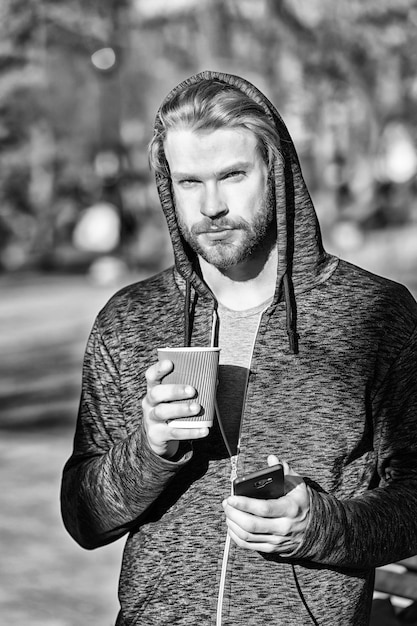 Hombre sujetando un teléfono móvil y un vaso de papel en el parque