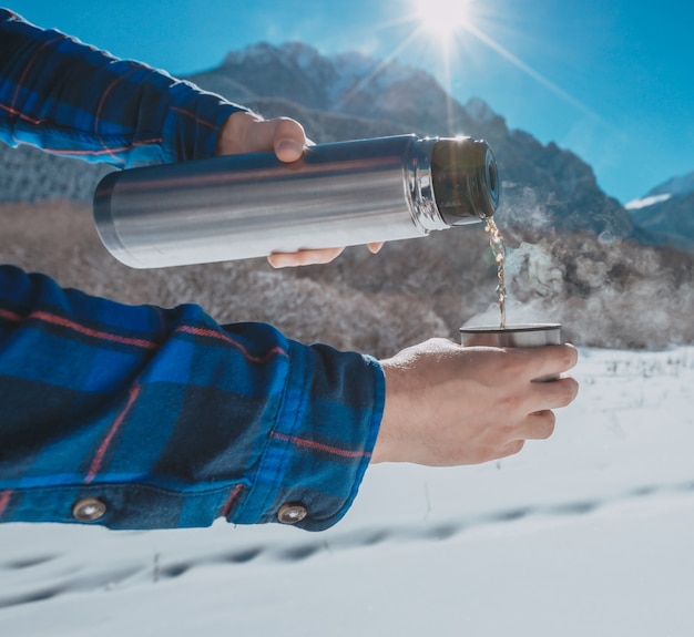 Hombre sujetando un termo en una montaña nevada