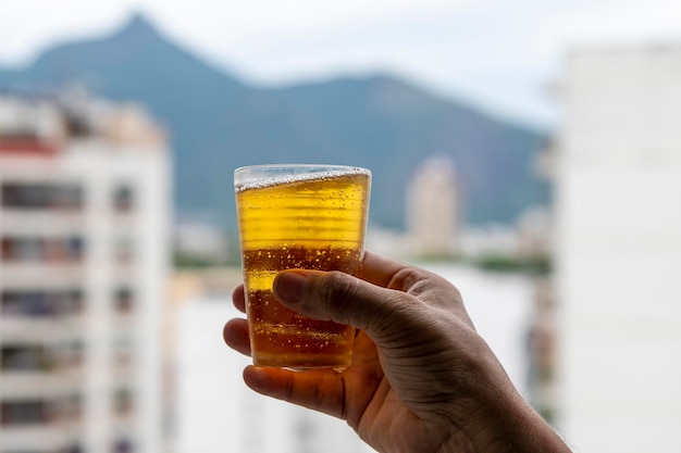 Hombre sujetando un vaso de cerveza en el fondo borroso de la ciudad urbana