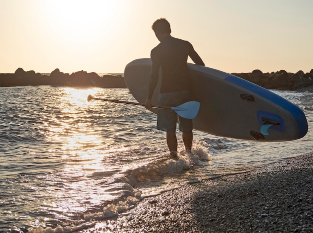 El hombre con SUP y remo en la playa va a surfear en el fondo dorado del atardecer