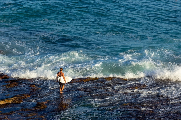 Hombre surfista llevando su tabla de surf y esperando las olas en el océano