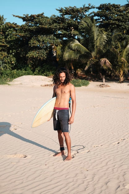 Hombre surfista sentado en la tabla de surf en la playa de arena