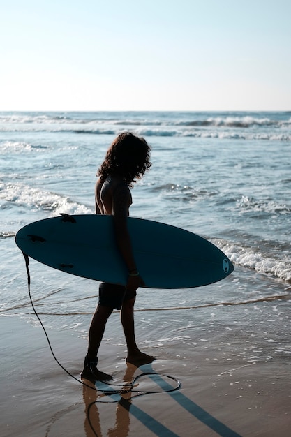 Hombre surfista sentado en la tabla de surf en la playa de arena