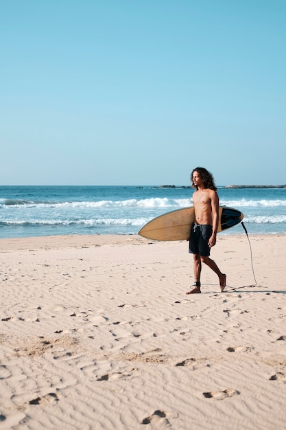 Hombre surfista sentado en la tabla de surf en la playa de arena