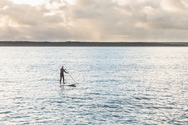 Hombre con tabla de paddle sobre los acantilados.