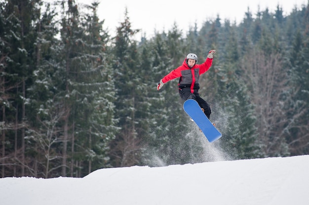 Hombre en la tabla de snowboard saltando sobre la pendiente en invierno