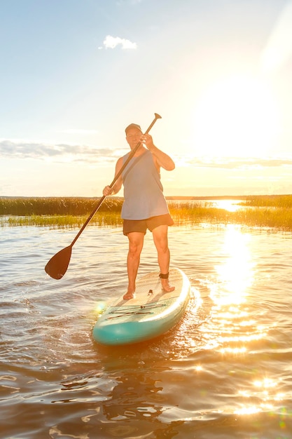 Un hombre en una tabla de SUP con un remo flota en el agua contra el fondo de la puesta de sol