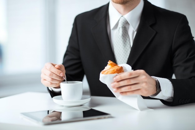 hombre con tablet pc, taza de café y croissant