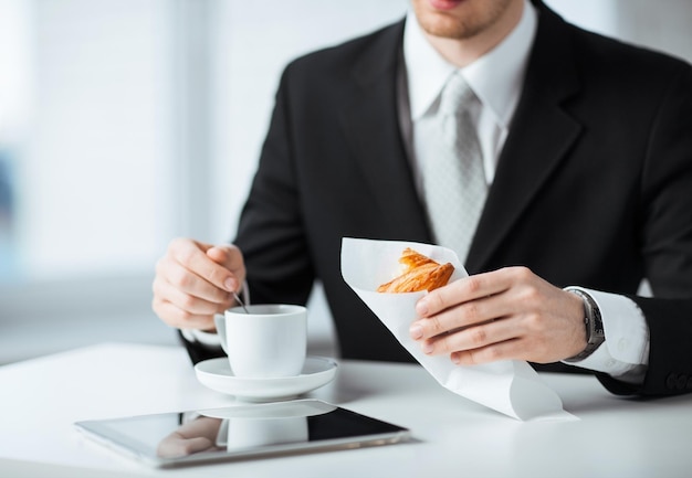 hombre con tablet pc, taza de café y croissant